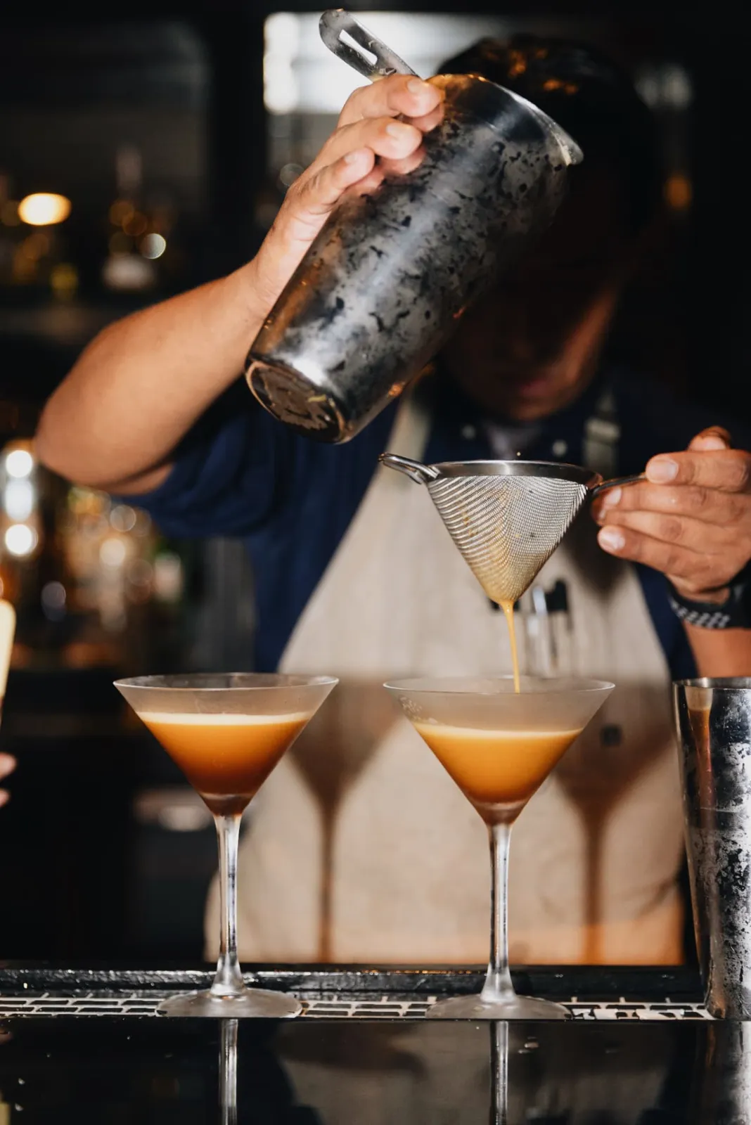 A bartender straining espresso martinis at the bar
