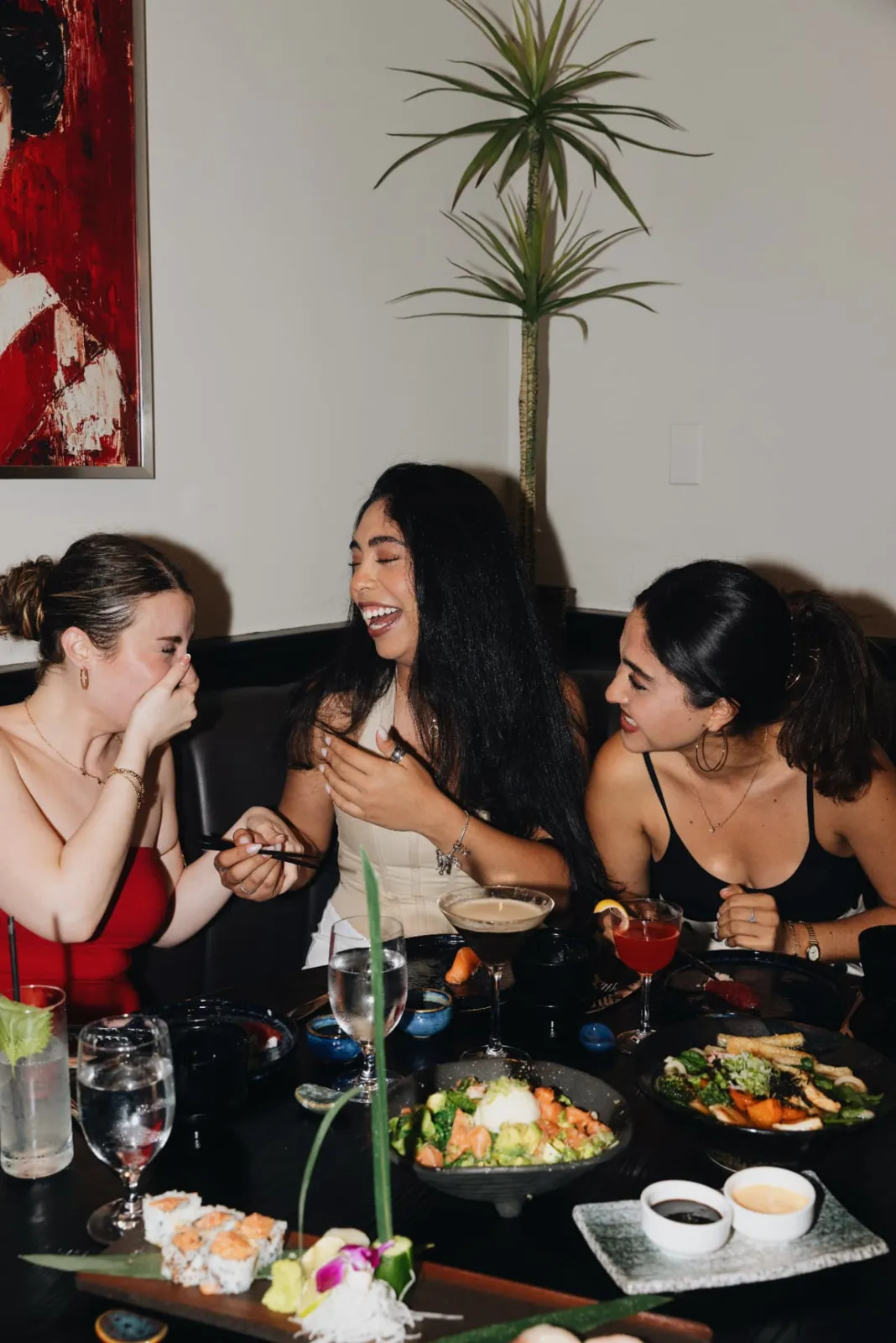 Friends laughing over sushi and cocktails in a booth